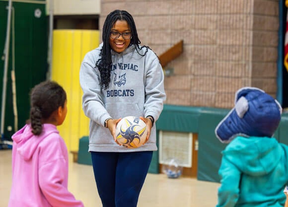 Student-athlete showing elementary students how to play rugby