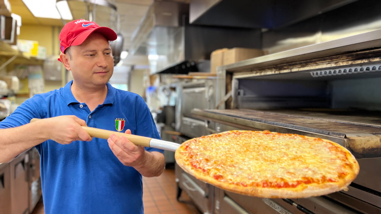 Gino of Tonino's pizza removes a cheese pie from the oven