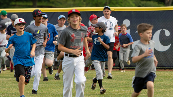 Dozens of kids laugh and run across the Quinnipiac baseball field