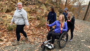 A person in a wheelchair goes for a hike with a group of people on a fall day