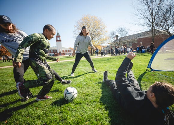 A child in a costume dribbles a soccer ball on the Quinnipiac quad as he plays with student-athletes