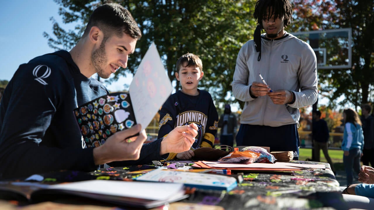 Quinnipiac students helping child make a Halloween card with stickers