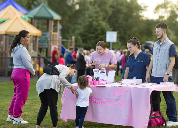 Three students talk with a family in a Hamden park during a breast cancer awareness event