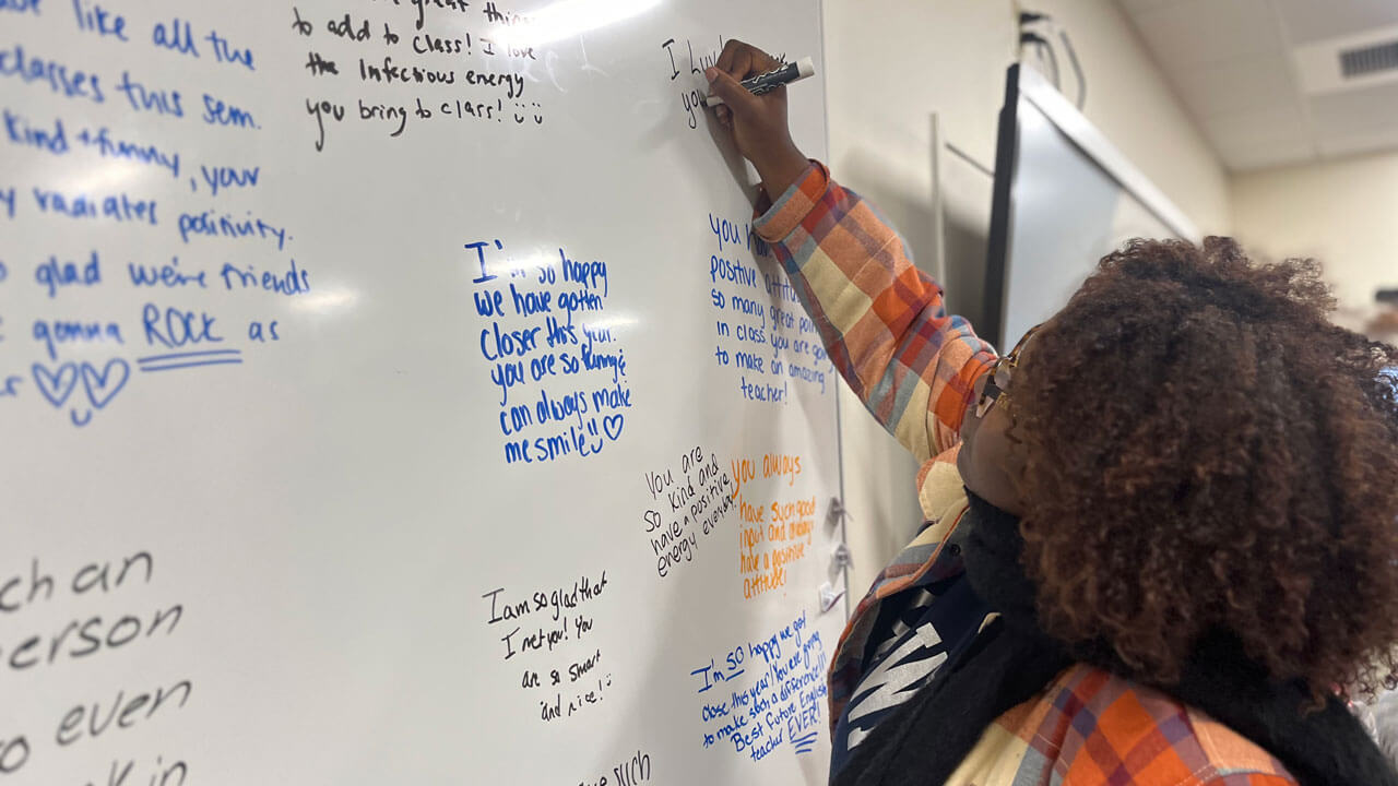 A student writes positive comments on a white board.