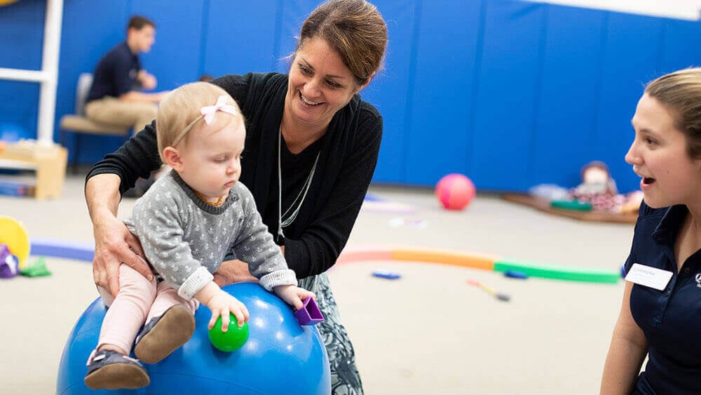A health sciences professor balances a baby on an exercise ball during a community outreach event