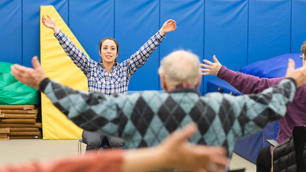 A health sciences student leads a group of senior citizens in stretching exercises