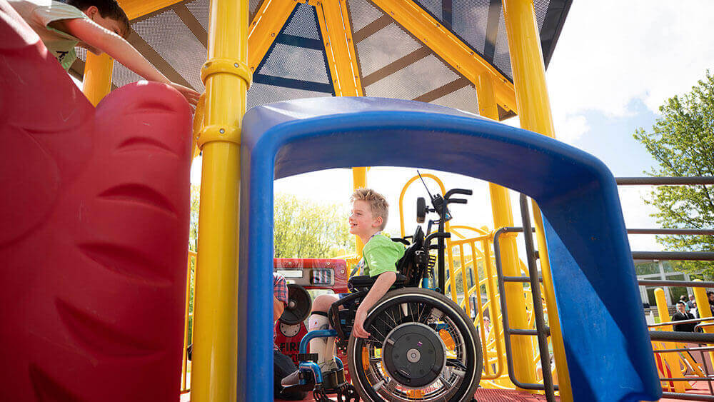 A young boy in a wheelchair plays on a local playground
