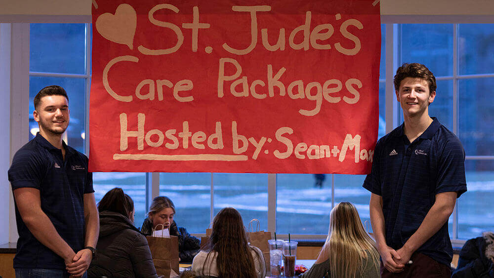 Two Quinnipiac students stand in front of a red St. Jude's fundraiser sign